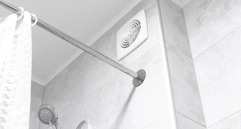 A modern bathroom features a ceiling exhaust fan, showerhead, and curtain rod against light gray tiles. 